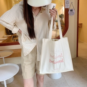 Detail of white canvas tote bag with pink beloved embroidery in a cafe setting