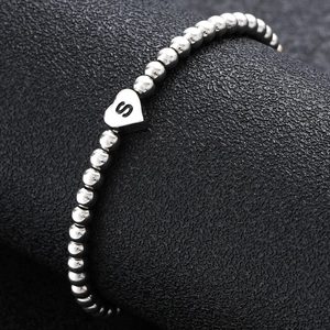 Macro shot of silver beaded bracelet with heart charm featuring a black letter S engraving