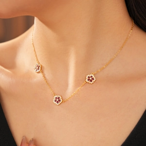 Primo piano della collana placcata oro 18K con tre fiori in zircone rosso su una modella