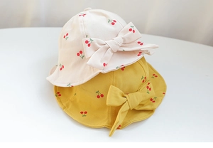 Close-up of yellow and beige baby bucket hats with cherry prints and decorative bows