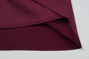 Close-up of double-stitched hem on burgundy satin dress showing refined fabric texture