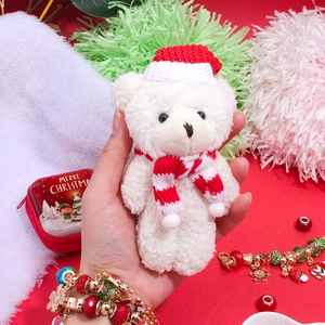 Gros plan d'un ours en peluche de Noël avec écharpe et bonnet rouge en main