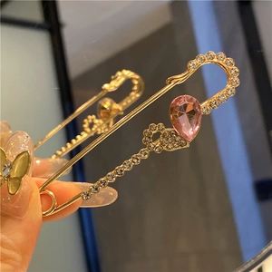 Detailed view of hand holding a gold pin brooch with pink teardrop crystal and rhinestones