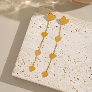 Detailed view of gold heart chain tassel earrings on a textured stone display pedestal