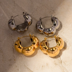Detailed close-up of gold and silver triple ball hoop earrings on light stone texture