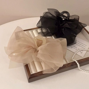 Close-up of elegant black and beige chiffon mesh bow hair claws on a wooden tray