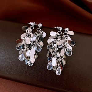 Detailed view of silver tassel earrings with clear crystals on dark leather texture
