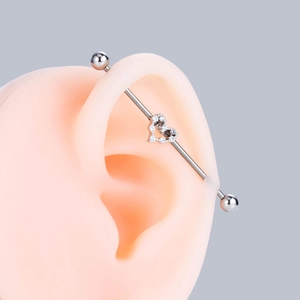 Silver industrial barbell piercing with crystal heart ornament on a silicone ear model