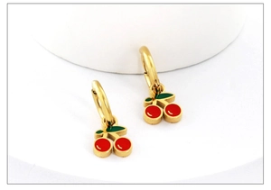 Close-up of bright red cherry earrings with green leaves on a white stand