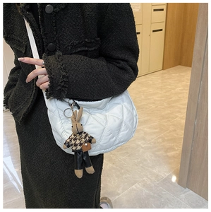 Detailed view of a white quilted shoulder bag featuring a cute brown rabbit charm on a model