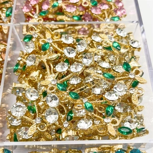 Close-up of bulk gold cherry pendants with green and white zircons in a storage box