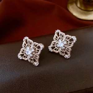 Macro detail of rose gold hollow flower stud earrings with white zircon on brown leather