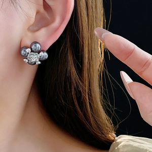 Detail of flower shaped earrings featuring dark grey pearls and zircons on a model
