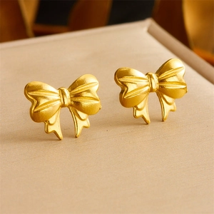 Close-up of gold bow earrings with matte texture on a soft beige jewelry box lining