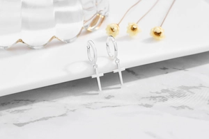 Macro shot of silver cross pendant earrings on white marble surface with dry flowers
