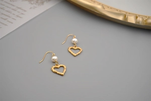 Detail shot of heart-shaped gold earrings with white freshwater pearls and hook back