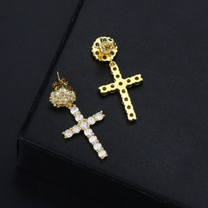 Makro-Detail von goldenen Kreuzohrringen mit Zirkonia auf schwarzer strukturierter Fläche