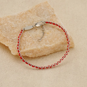 Detailed close-up of red braided string bracelet with silver beads and lobster clasp