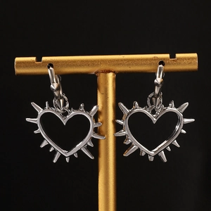 Detailed view of silver punk heart earrings with thorns on a golden display stand