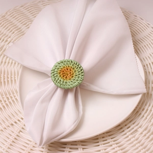 Detail of round handmade rattan napkin ring in natural green and wood tones on white linen