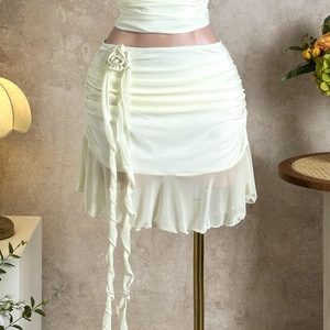 Detail of cream white mini skirt with floral accent, pleats and ruffled hemline