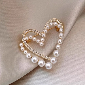 Elegant hollow heart brooch with white pearls and sparkling crystals on silk background