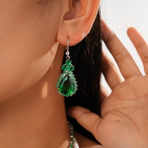 Close-up of green teardrop gemstone earrings with diamond pavé accents on a model