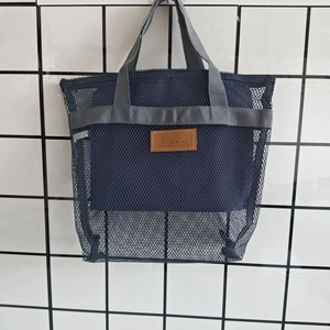 Dettaglio della borsa a rete blu scuro con manici grigi ed etichetta in pelle marrone