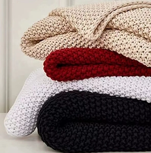 Detail of chunky knit blankets in beige, red, white and black with thick wool texture