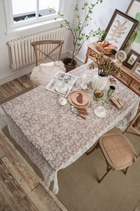 Detailed top view of white floral lace tablecloth on a beige base fabric in a dining room