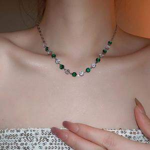 Detailed close-up of a silver necklace with alternating green and white cubic zirconia