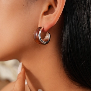 Detail of a brown resin C-shape earring with silver metal lining worn by a model