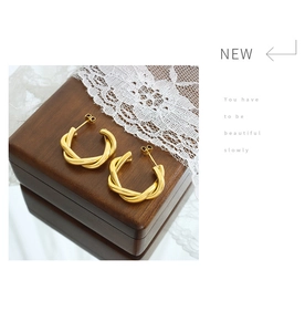 Detail view of 18K gold-plated C-shaped twist earrings on a wooden jewelry box