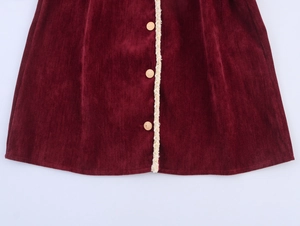 Close-up of burgundy chenille dress hem with gold buttons and white fringe trim