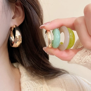 Close-up of golden hoop earrings and colorful resin hoops in mint green and transparent grey