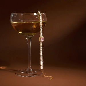 Détail d'un bracelet tennis en acier doré avec zircon rose sur un verre à vin