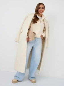 Close-up of minimalist cream wool coat paired with half-zip hoodie and blue jeans