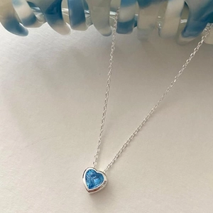 Macro detail of silver heart necklace featuring a vibrant blue faceted zircon gemstone