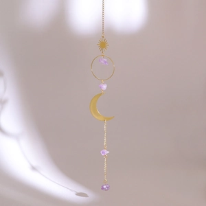 Detail of amethyst suncatcher with golden sun and moon pendants on beige wall