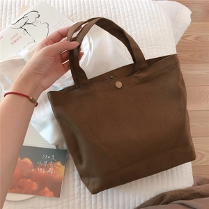 Detail of a dark brown canvas handbag featuring a secure metal snap button closure