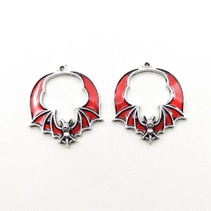 Detailed view of two vintage bat pendants featuring red enamel and silver alloy metal