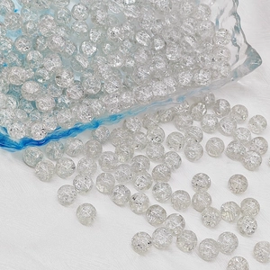 Macro shot of 6mm-8mm round crackle glass beads spilling onto a white background