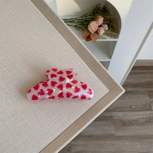 Close-up of translucent pink heart-patterned hair claw clip on soft beige fabric