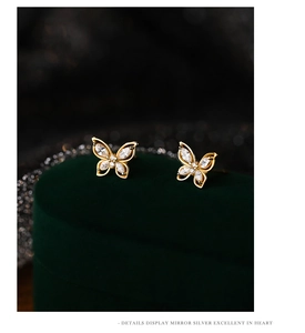 Macro detail of golden butterfly earrings with zircons on a green velvet jewelry box
