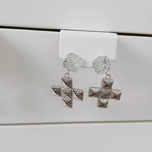 Close-up of silver steel cross earrings featuring square studs and spiral textured centers