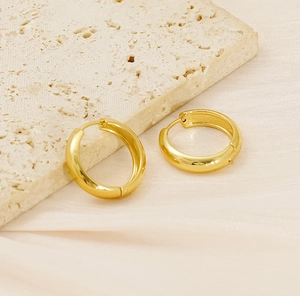 Close-up of polished 18K gold plated stainless steel hoop earrings on a stone base