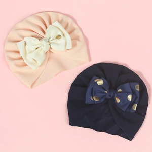Detail of pink and navy baby turban hats featuring gold polka dot ribbon bows and crinkle fabric