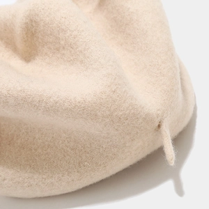 Close-up of the beige wool fabric texture and small tail detail on a retro beret hat