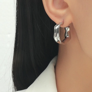 Close-up of geometric C-shaped silver earrings with twisted metal texture on female model