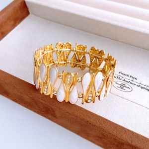 Macro detail of golden teardrop bangle with zircon inlay and white enamel in a gift box